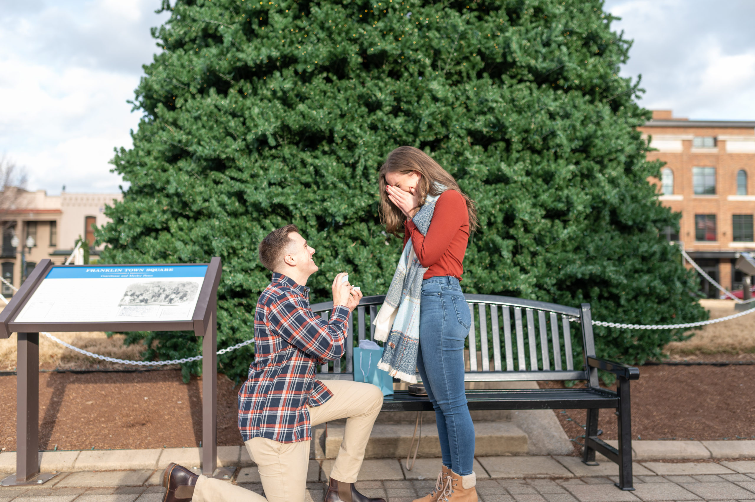 A man on one knee as he proposes to his girlfriend in front of the Christmas tree in Downtown Franklin, TN.