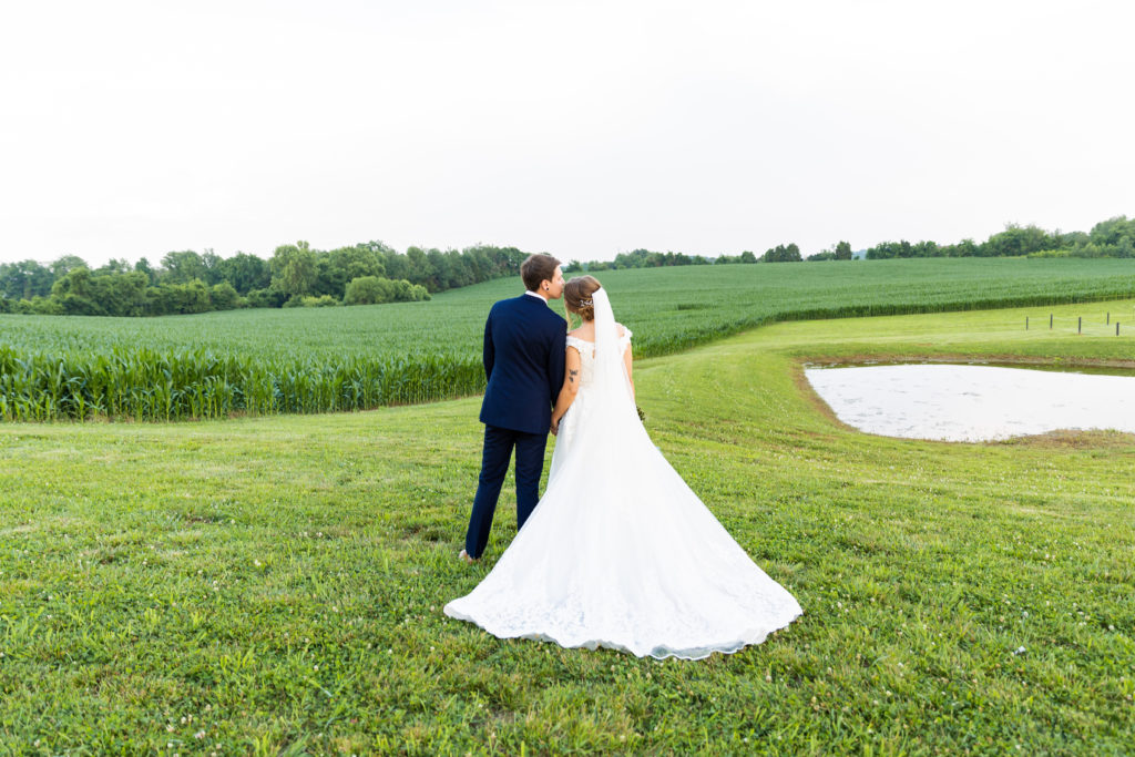 Outdoor bride and groom portrait in field near pond