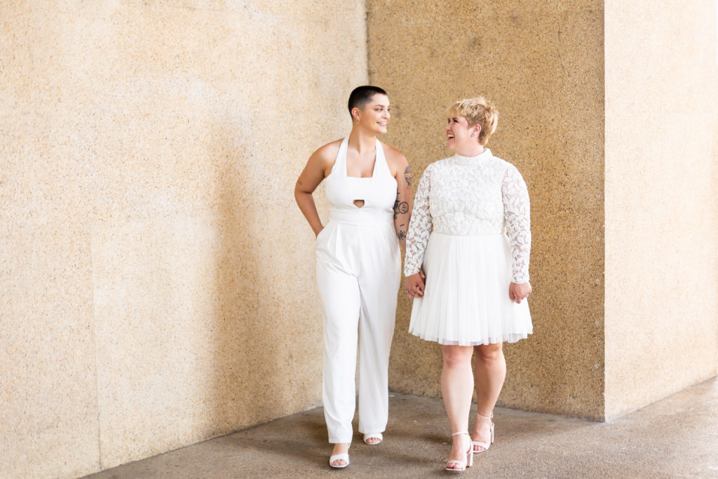 Bride wearing jumpsuit and bride wearing dress walking and holding hands 