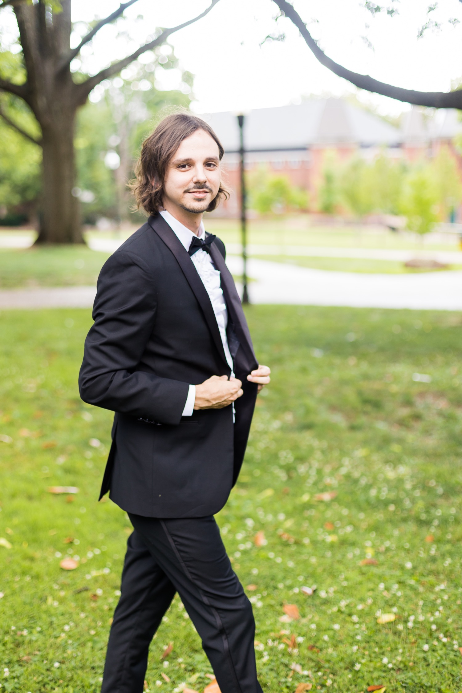 The groom looking at the camera as he walks buttoning his tuxedo jacket