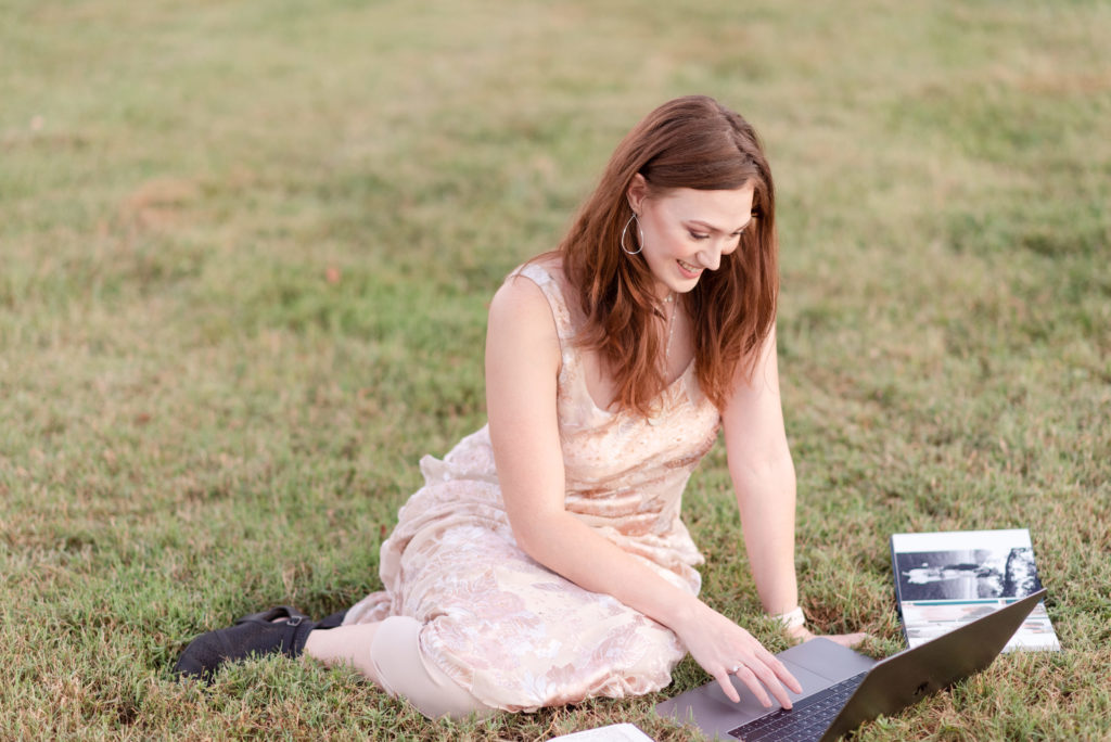woman in dress sitting in grass with laptop