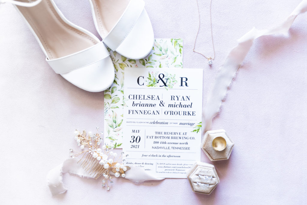 white wedding detail shot with rings, invitations, and shoes
