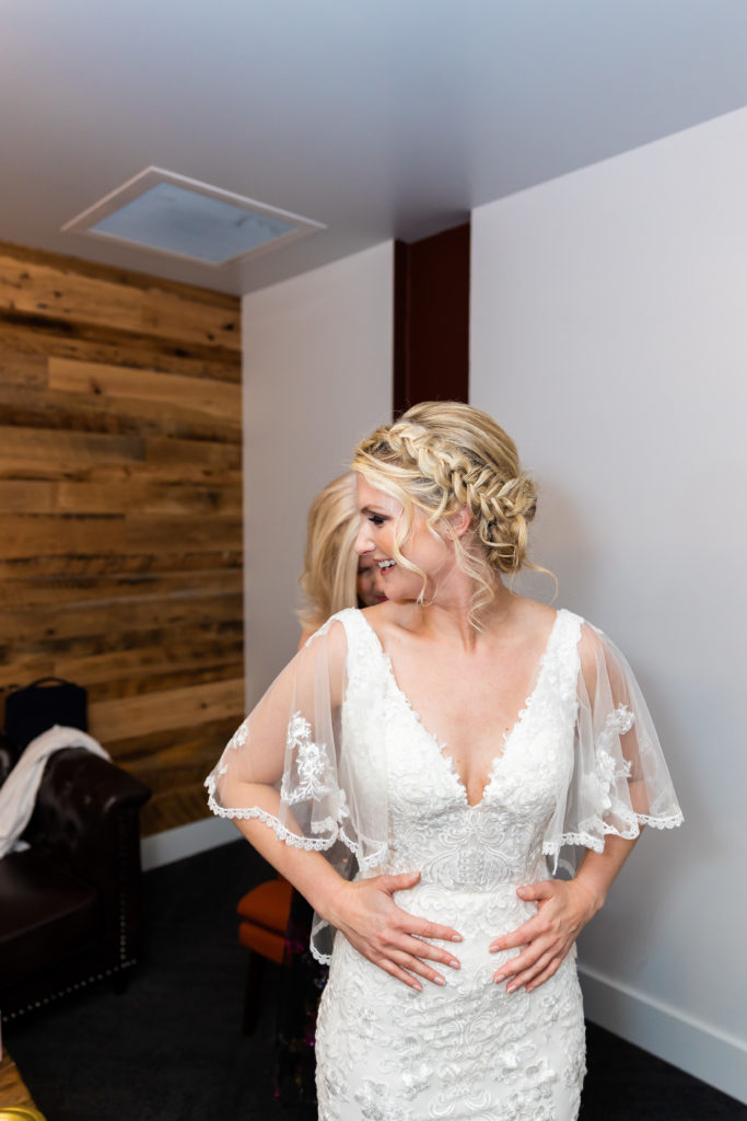 Bride getting zipped into dress by mom