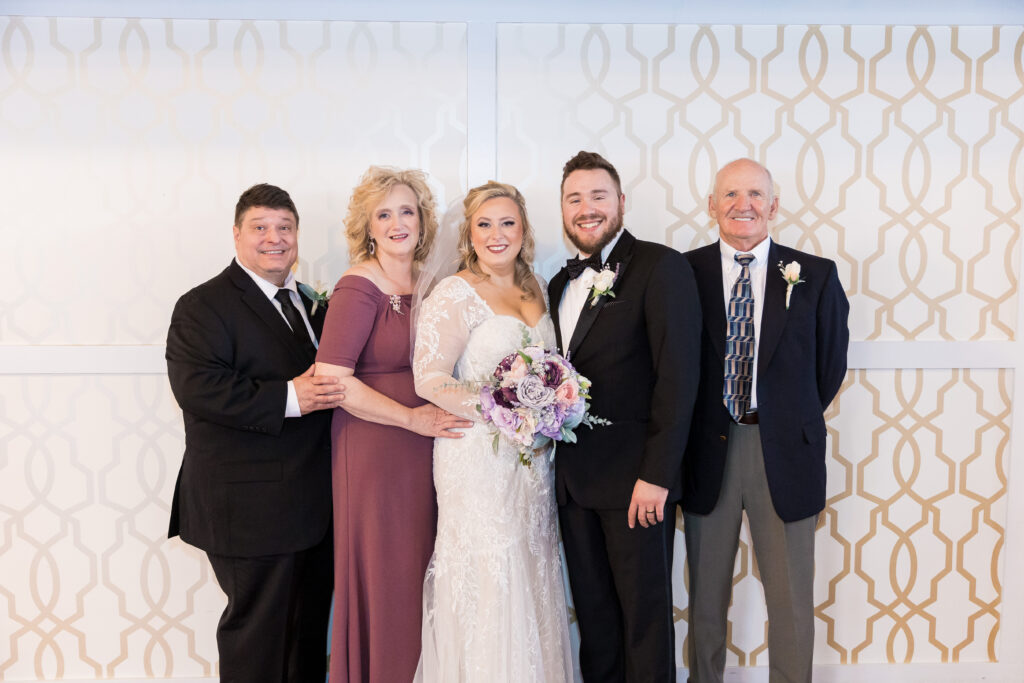 A bride and groom smile with the bride's parents and grandfather on their wedding day during family formals.