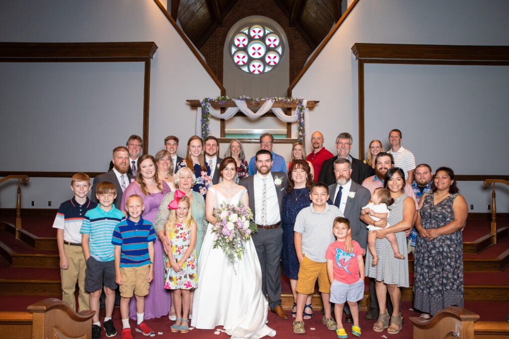 A bride and groom smile during an extended family portrait on their wedding day.