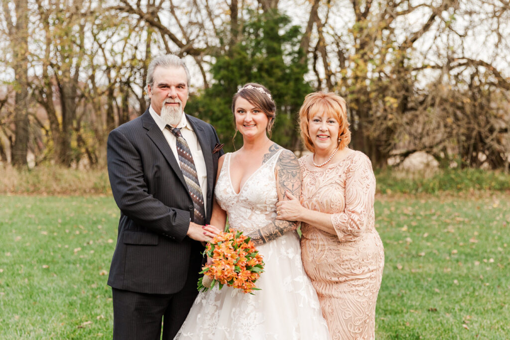 A November bride smiles with her parents on her wedding day.